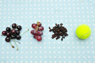 Small bunches of cherries and grapes, and a pile of raisins next to a tennis ball